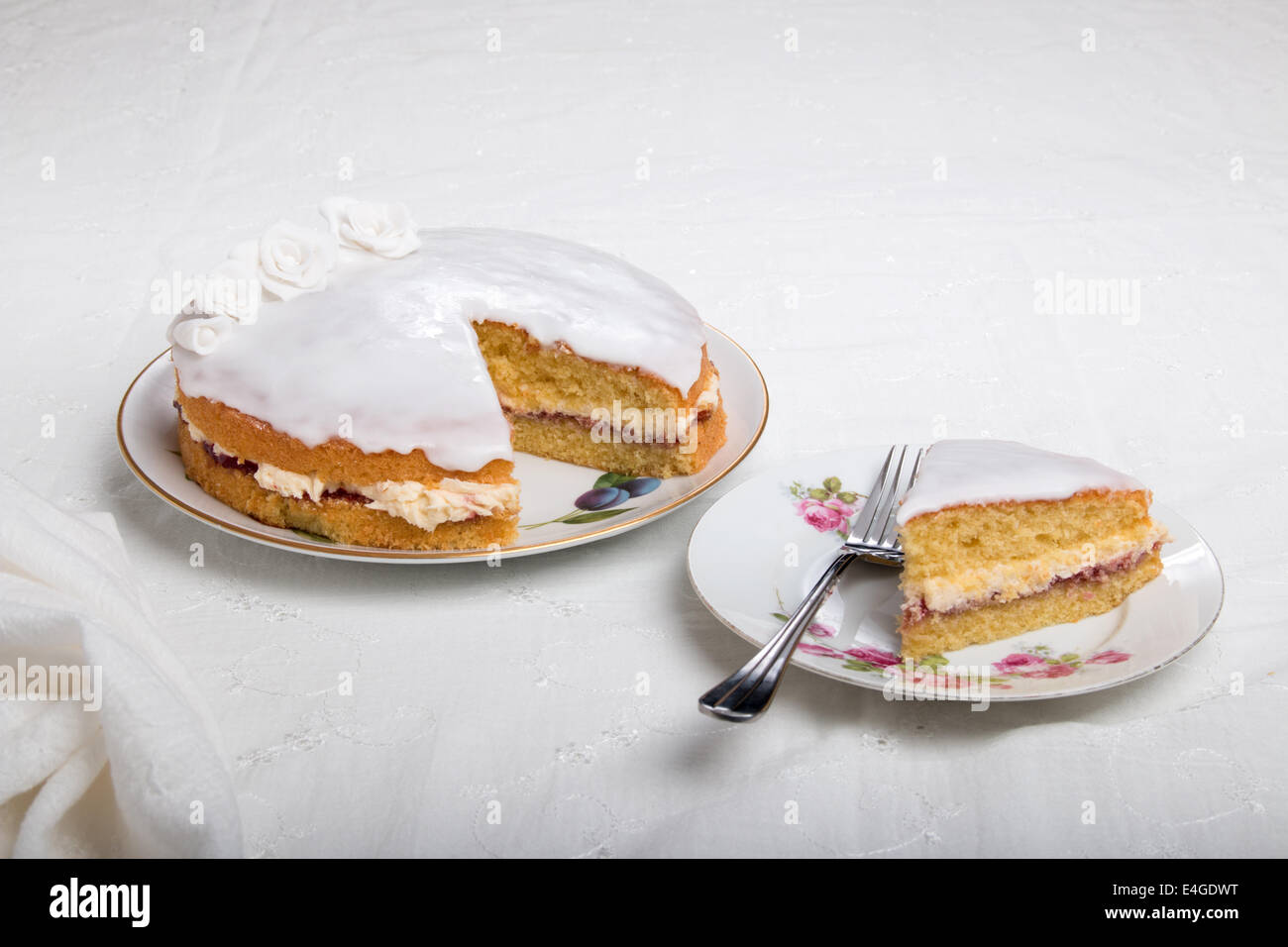Victoria-Biskuit Eistee in weiß mit handgemachten Rosen auf einem Teller Kuchen auf einem Teller neben (44a von 44) Stockfoto