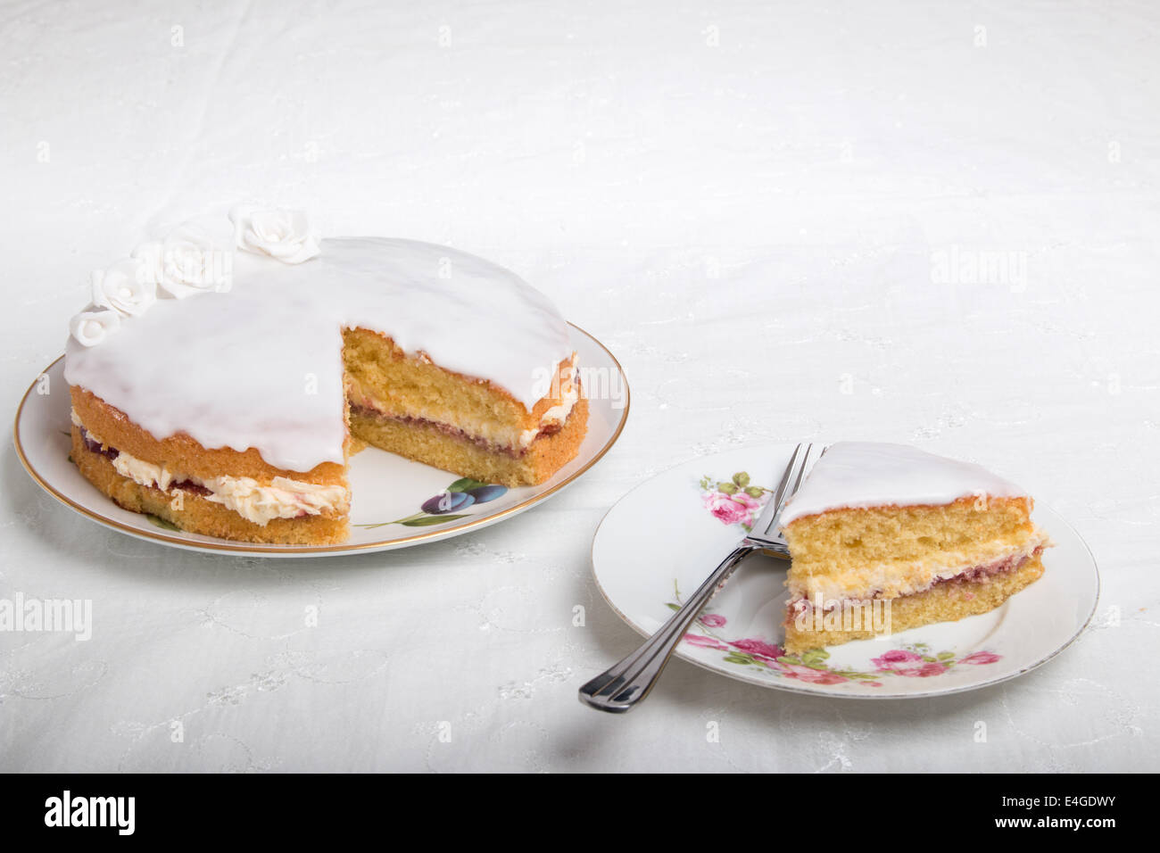 Victoria-Biskuit Eistee in weiß mit handgemachten Rosen auf einem Teller Kuchen auf einem Teller neben (35 von 44) Stockfoto