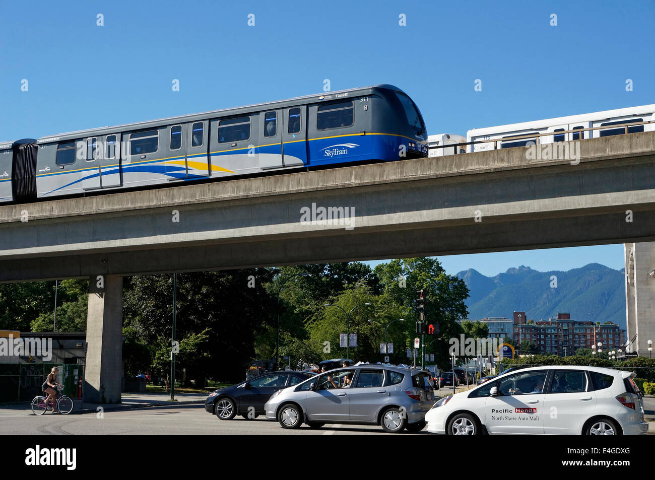 Der Skytrain erhöhte helle schnelle Durchfahrt System überqueren einer viel befahrenen Straße mit Autos und ein Fahrrad, Vancouver, BC, Kanada Stockfoto