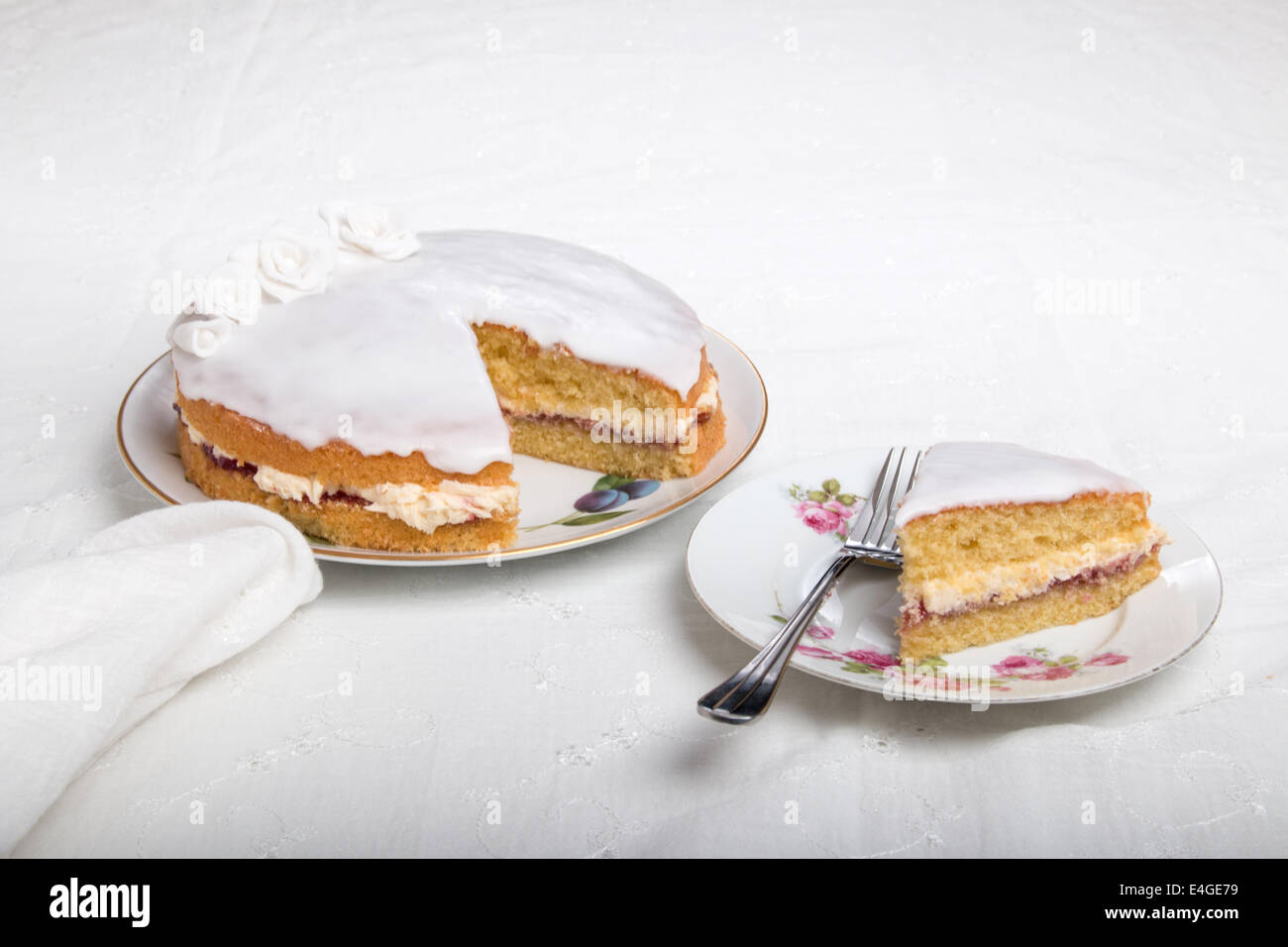 Victoria-Biskuit Eistee in weiß mit handgemachten Rosen auf einem Teller Kuchen auf einem Teller neben (44 44) Stockfoto