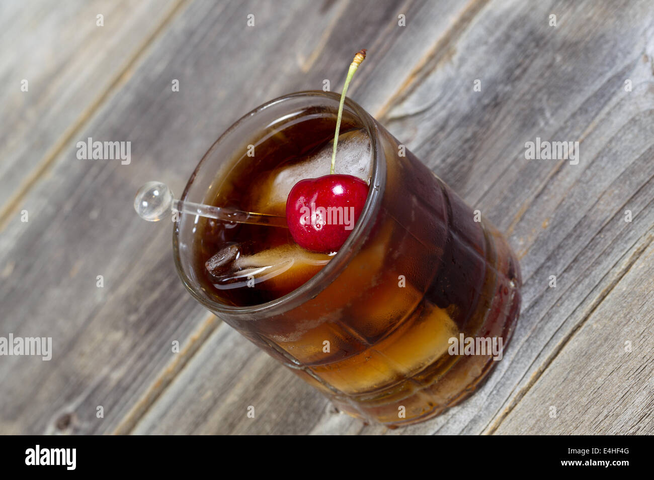 Horizontalen abgewinkelten Detailansicht einer Rum und Cola mit großen roten Kirschen und Eis im Glas Position auf rustikalen Holz Stockfoto