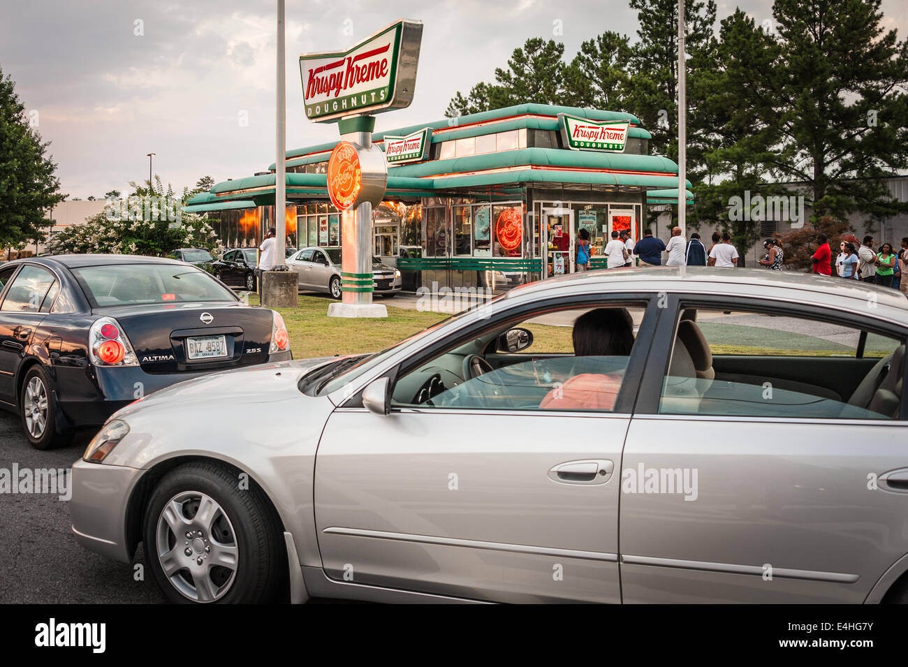 Lange Schlangen von Kunden, beide stehen und in Autos, warten geduldig für den süßen Geschmack des Südens, Krispy Kreme Doughnuts. Stockfoto