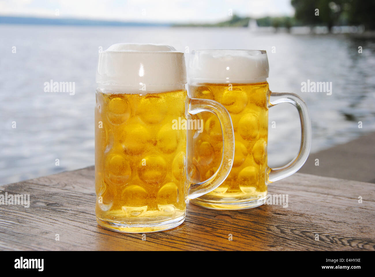 zwei Bierkrüge mit frischem Bier und Schaum auf einem Holztisch im Biergarten am See, Nahaufnahme Stockfoto
