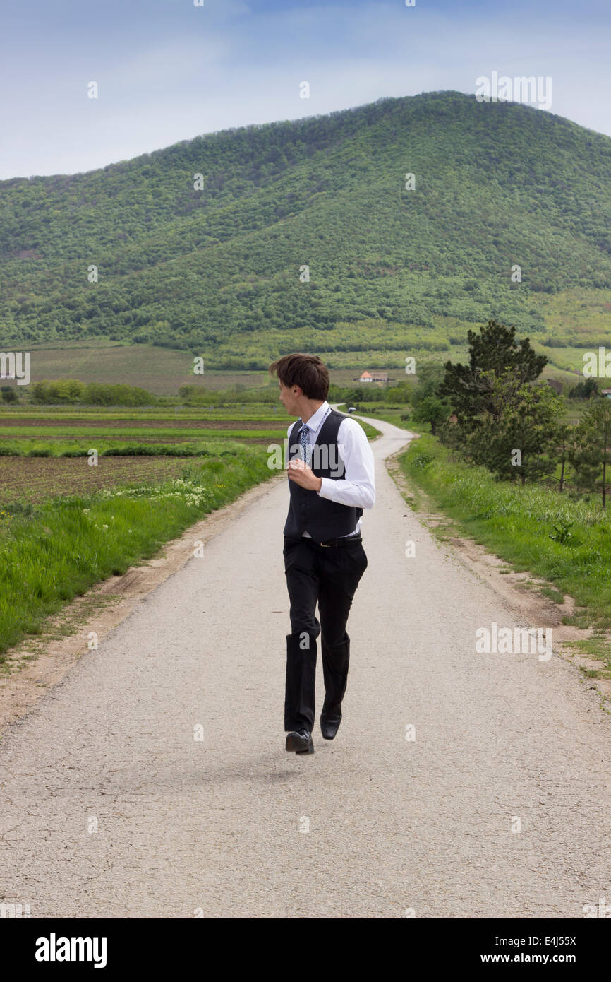 Geschäftsmann auf der Straße, auf der Suche über die Schulter der Bergstrasse hinter ihm. Laufen in Richtung Kamera, mal hängen Stockfoto