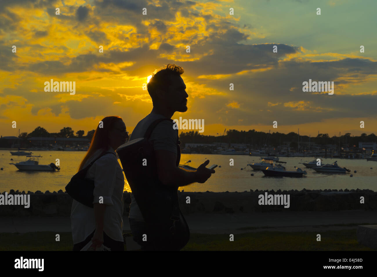 Port Washington, New York, USA. 11. Juli 2014. Als die Sonne untergeht sind ein junger Mann und eine Frau in der Silhouette gesehen, wie sie in Sunset Park entlang Manhasset Bay mit Booten im Wasser, in das Dorf North Shore auf Long Island Gold Coast vor Anker gehen. © Ann Parry/ZUMA Draht/Alamy Live-Nachrichten Stockfoto