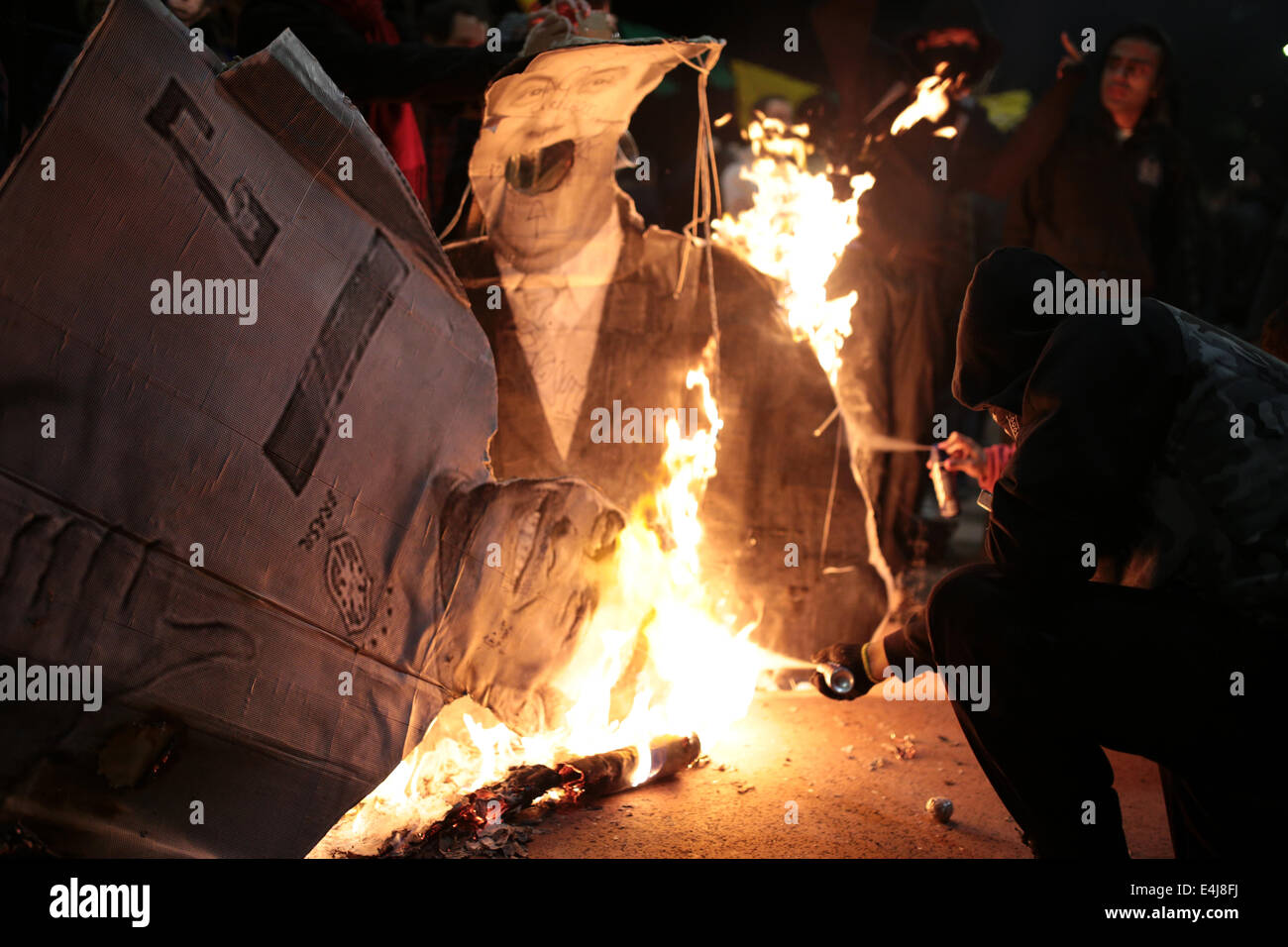 Sao Paulo, Brasilien. 12. Juli 2014. Ein maskierter Demonstrant verwendet ein Deodorant Spray um zu brennen Bilder der ehemalige brasilianische Fußballspieler Ronaldo und der Sekretär der Sicherheit von Sao Paulo, Fernando Grella während einer Protestaktion gegen die Inhaftierung von Aktivisten, die in einer früheren Demonstration gegen die FIFA WM 2014 in Roosevelt-Platz festgenommen wurden. Bildnachweis: Tiago Mazza Chiaravalloti/Pacific Press/Alamy Live-Nachrichten Stockfoto