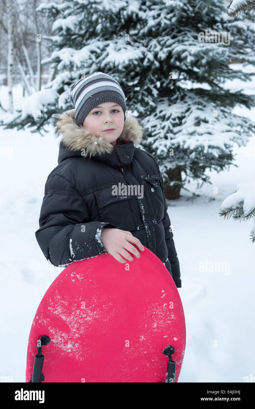 Junge in einem verschneiten Wald mit einem Schlitten Stockfoto