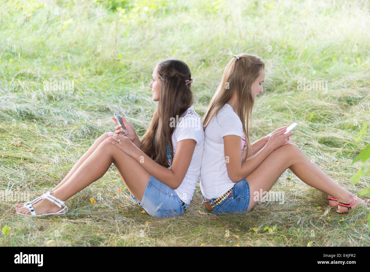 Zwei Mädchen im Teenageralter mit Handys sind auf dem Rasen sitzen. Stockfoto