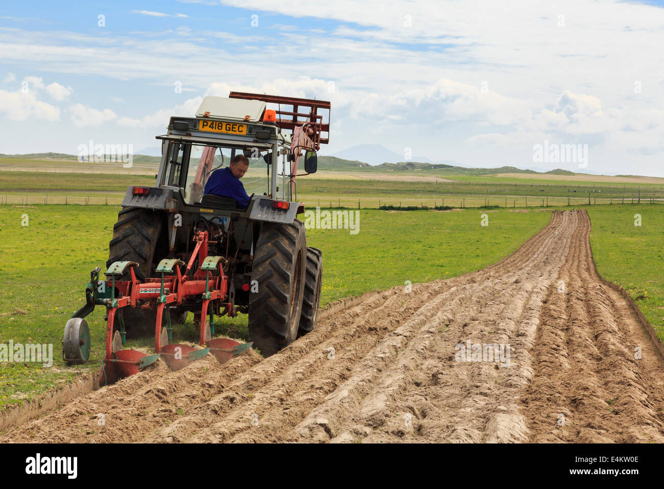 Croft Bauern pflügen Furchen in einem Feld der traditionellen Country Side machair Grünland mit einem Traktor Ziehen einer Pflugschar. Äußere Hebriden Schottland Großbritannien Stockfoto