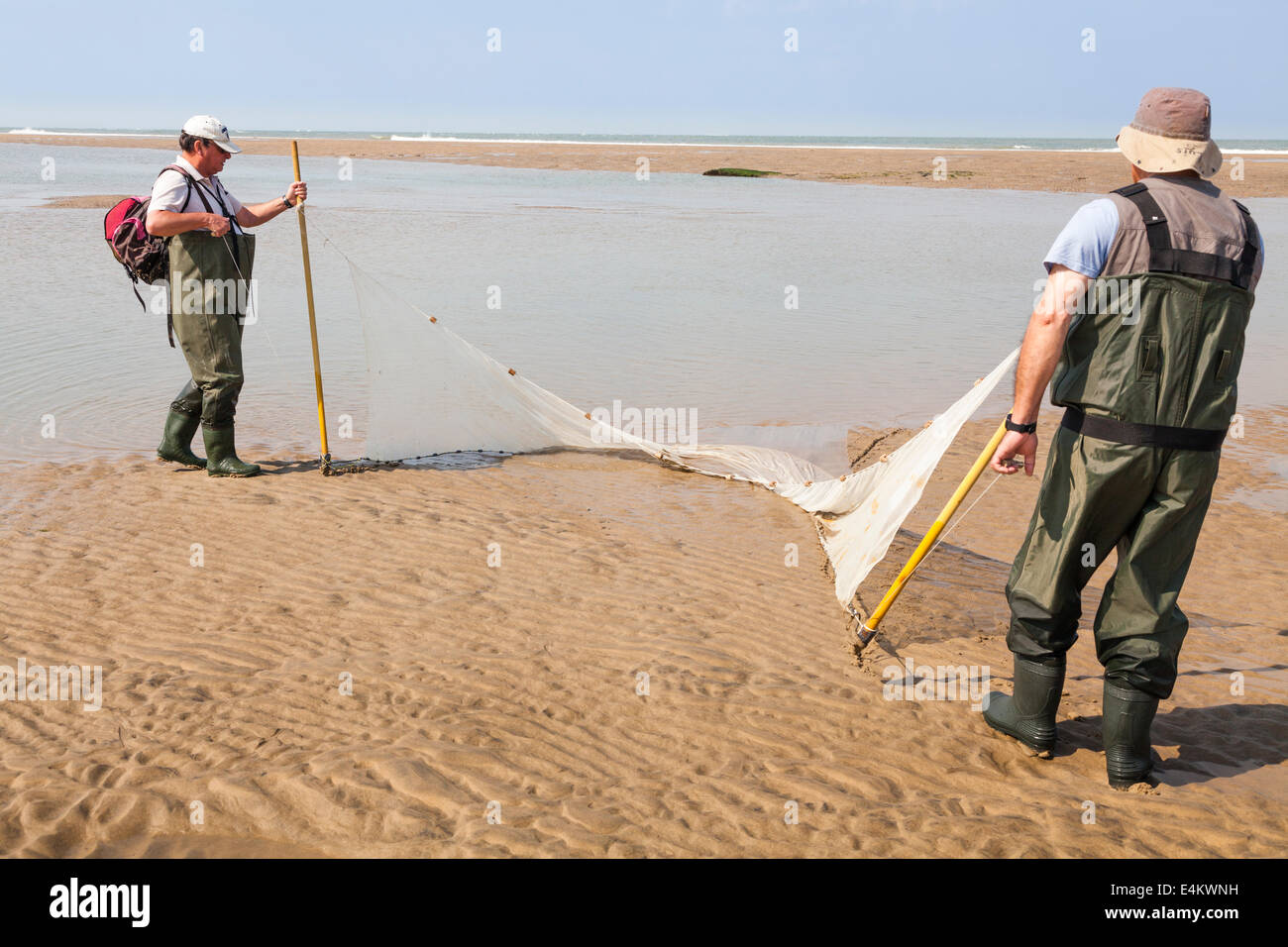 Zwei Fischer ziehen ihre Schleppnetz auf den Strand, wenn Schleppnetzfischerei für Fische in einem Pool von der zurückweichenden Flut verlassen. Stockfoto