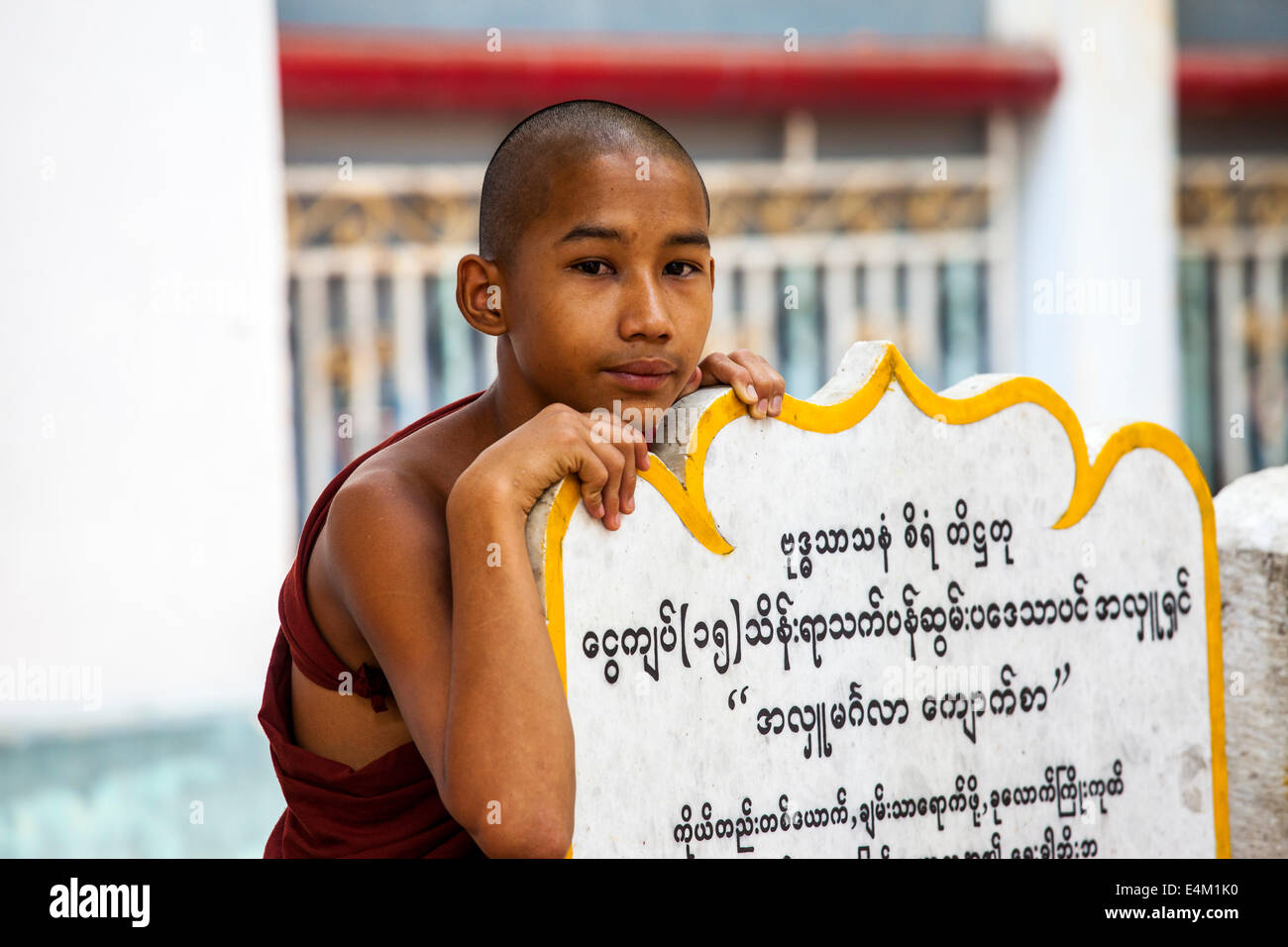 Ein junger Mönch ruht auf einem großen Tablett buddhistische Schrift, während er wartet, bis ein Almosen Zeremonie in Mandalay, Myanmar beginnen. Stockfoto