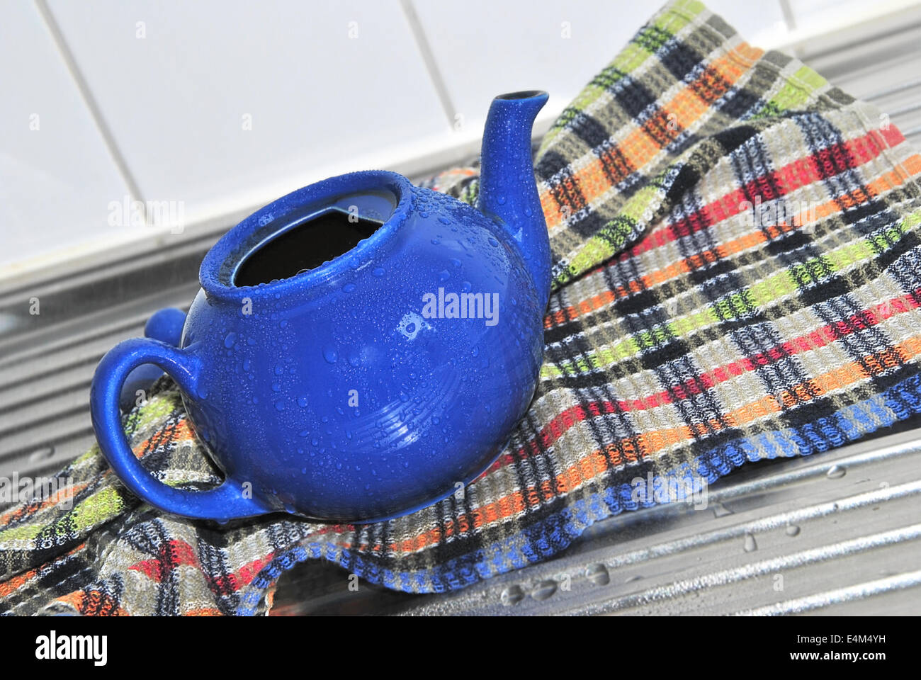 Teekanne mit Wassertropfen auf einem bunten karierten Küchentuch auf Küchenspüle blau, Nahaufnahme Stockfoto