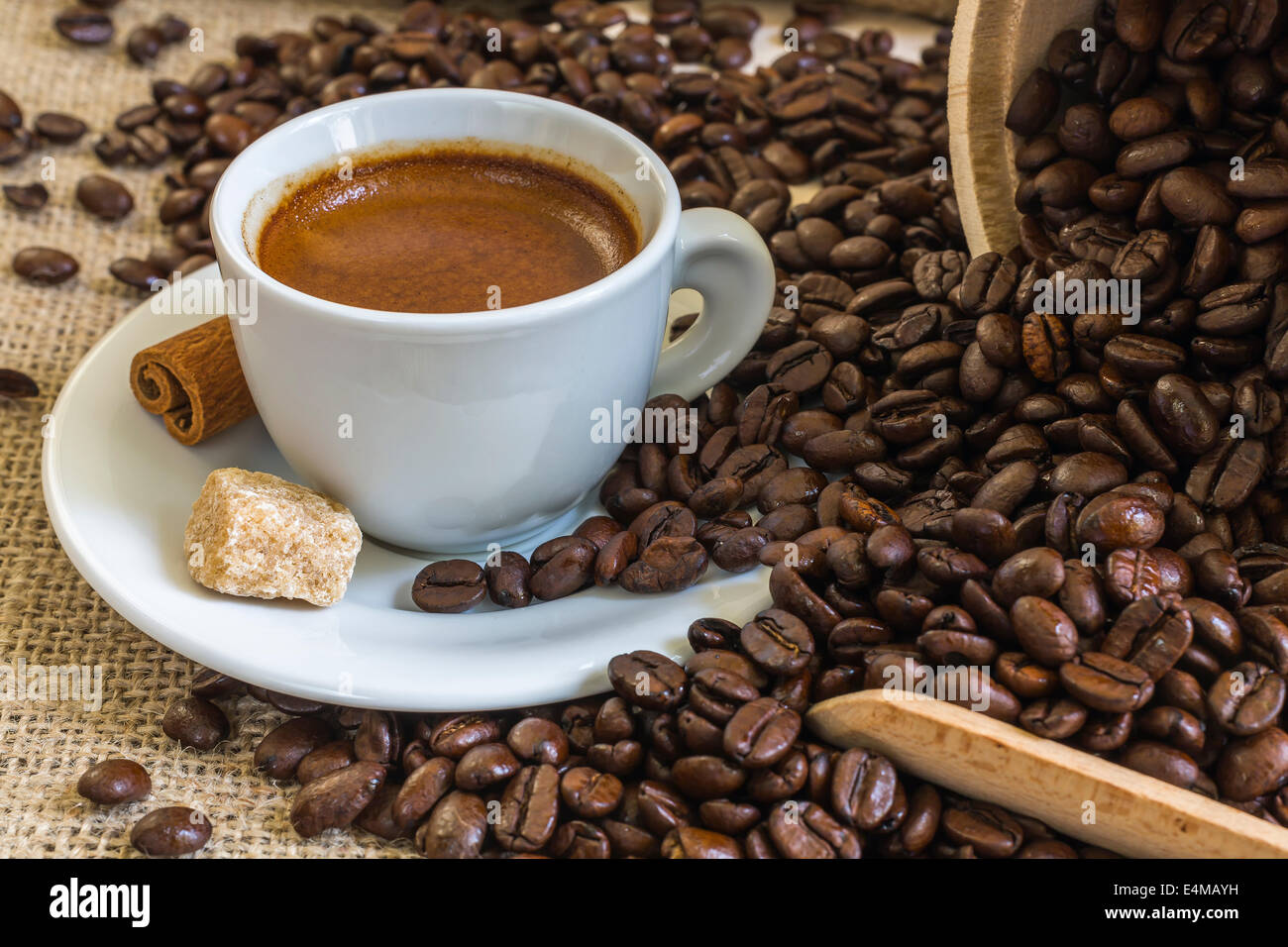 frischer Espressokaffee in weiße Tasse mit Würfelzucker, Zimt und gerösteten Kaffeebohnen auf Sackleinen Stockfoto