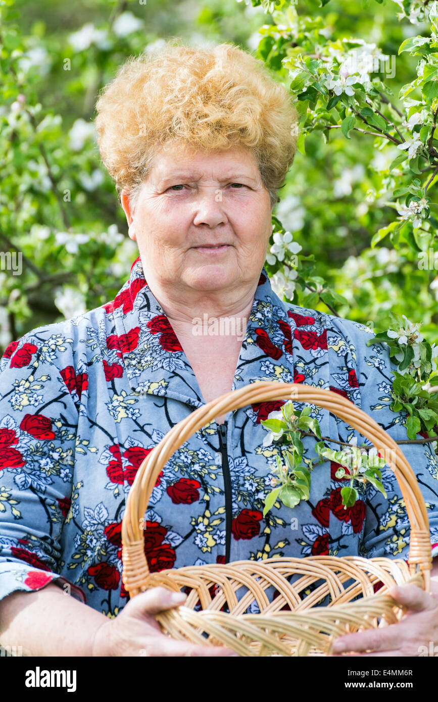 Reife Frau mit Weidenkorb im Frühlingsgarten Stockfoto
