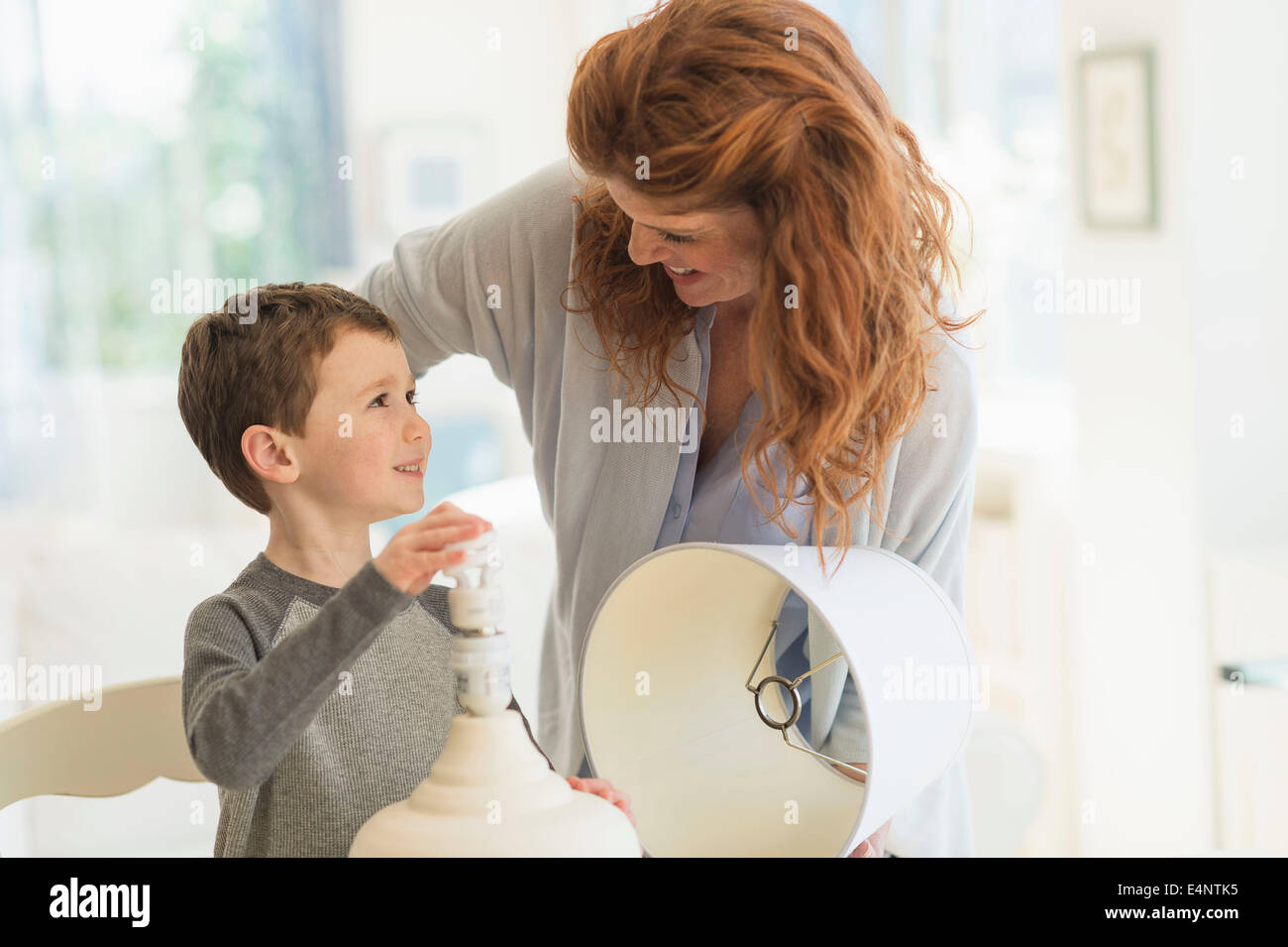 Sohn (6-7) und Mutter Wechsel Glühbirne in Tischleuchte Stockfoto