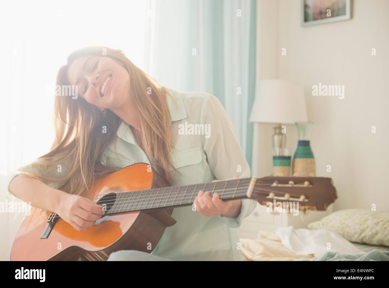 Junge Frau, die Akustik-Gitarre auf Bett Stockfoto