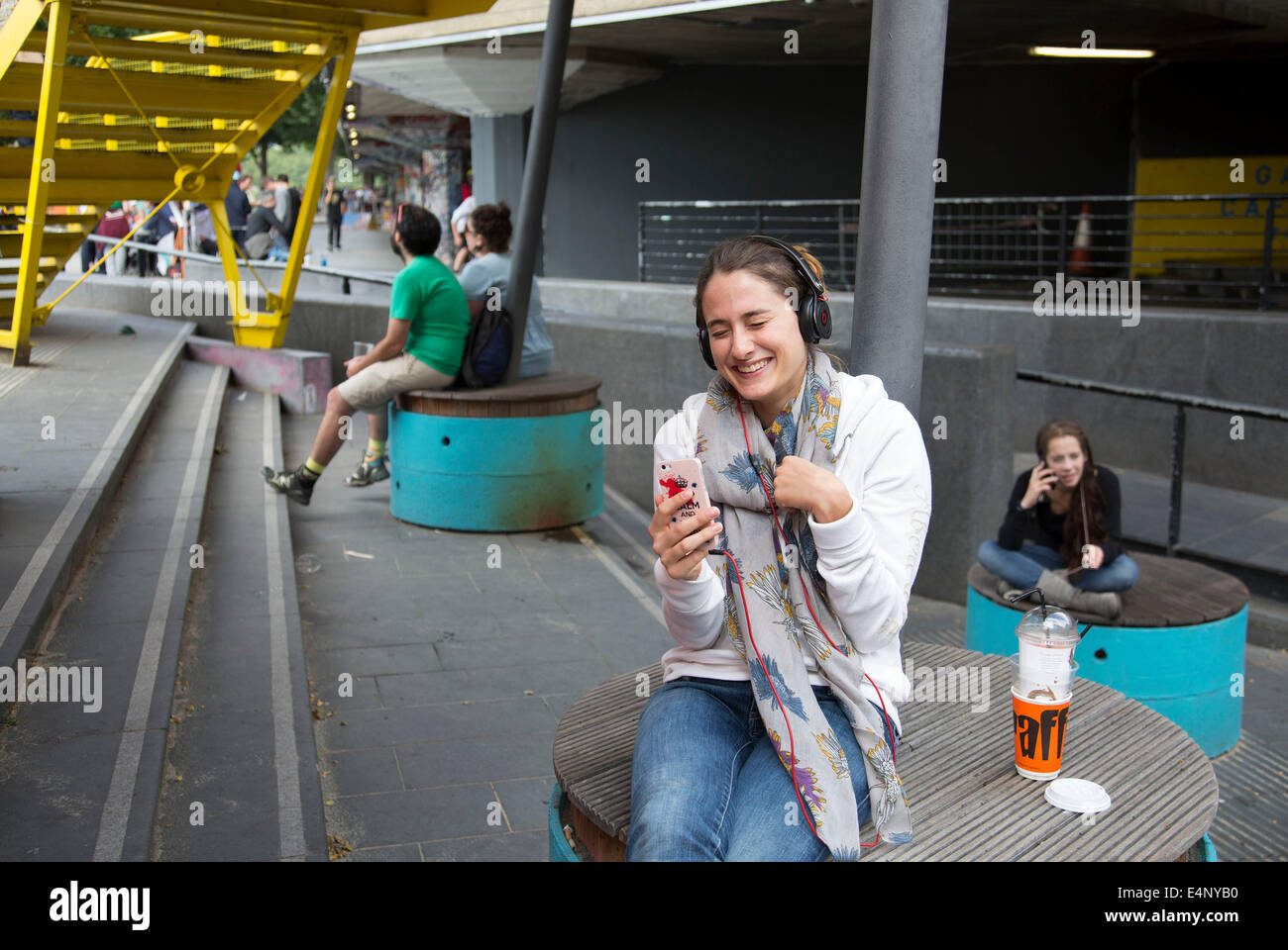 Junge Frau lächelt, während sie einen FaceTime-Anruf auf ihr Smartphone mit einem Freund genießt. South Bank, London, UK. Stockfoto