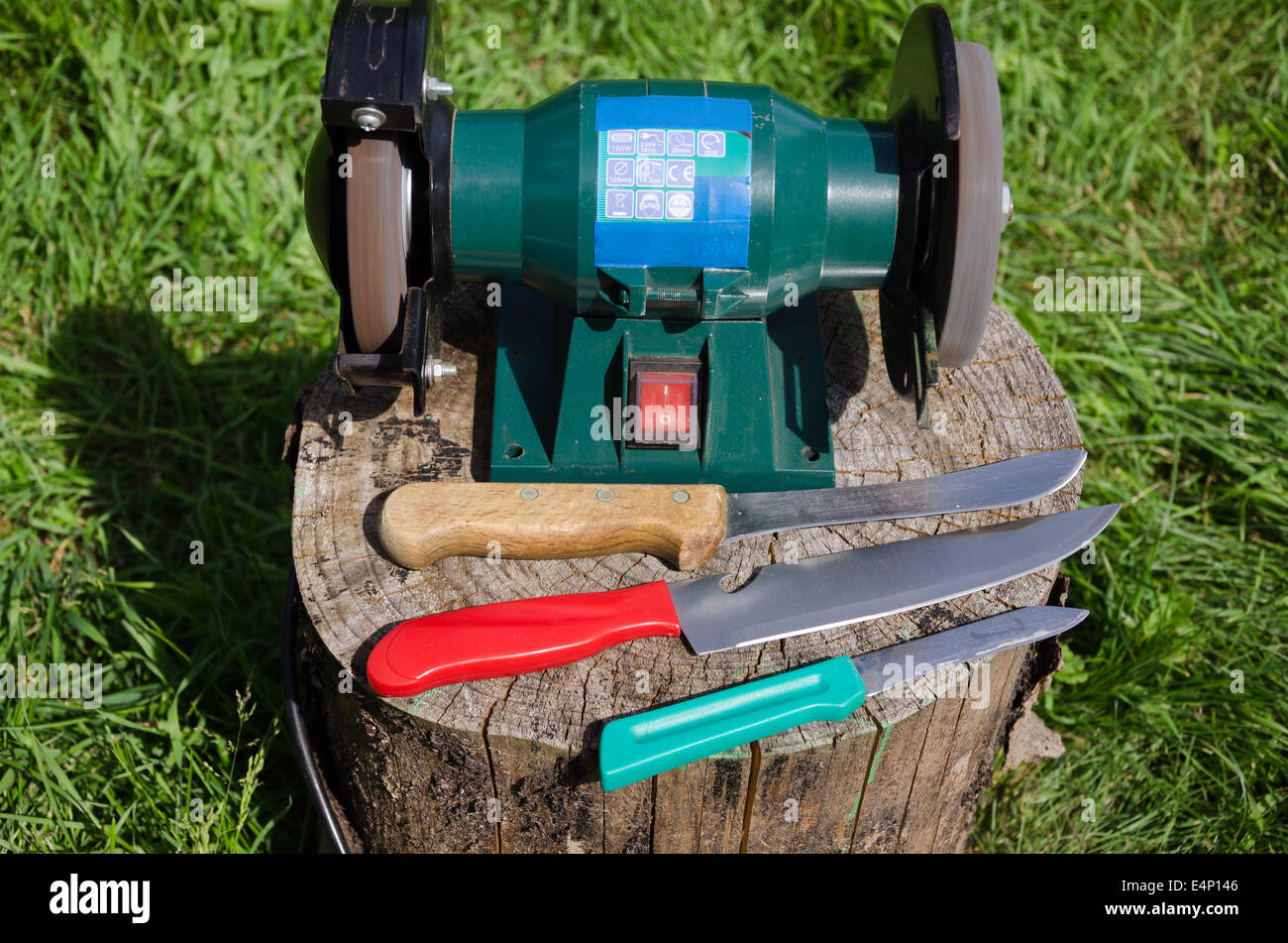 elektrische Messer schärfen Gerät und drei Küchenmesser auf Baumstumpf im freien Stockfoto