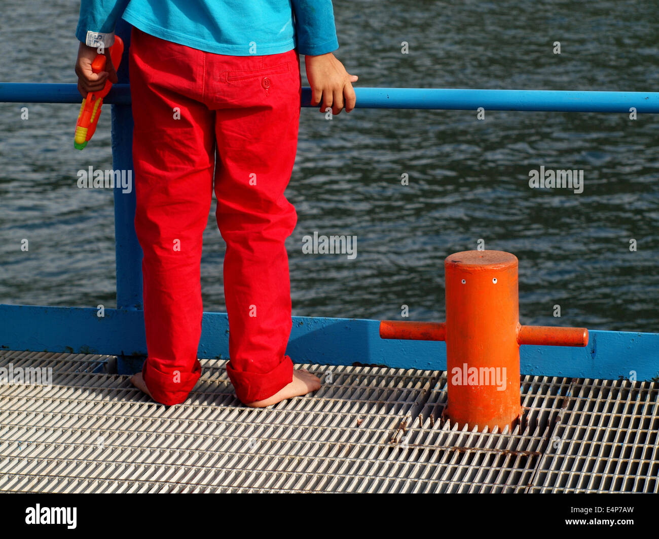 Helles Bild eines Jugendlichen mit roten Hosen und blauen oben an Deck des Schiffes Blick auf das Meer mit einer Wasserpistole Stockfoto
