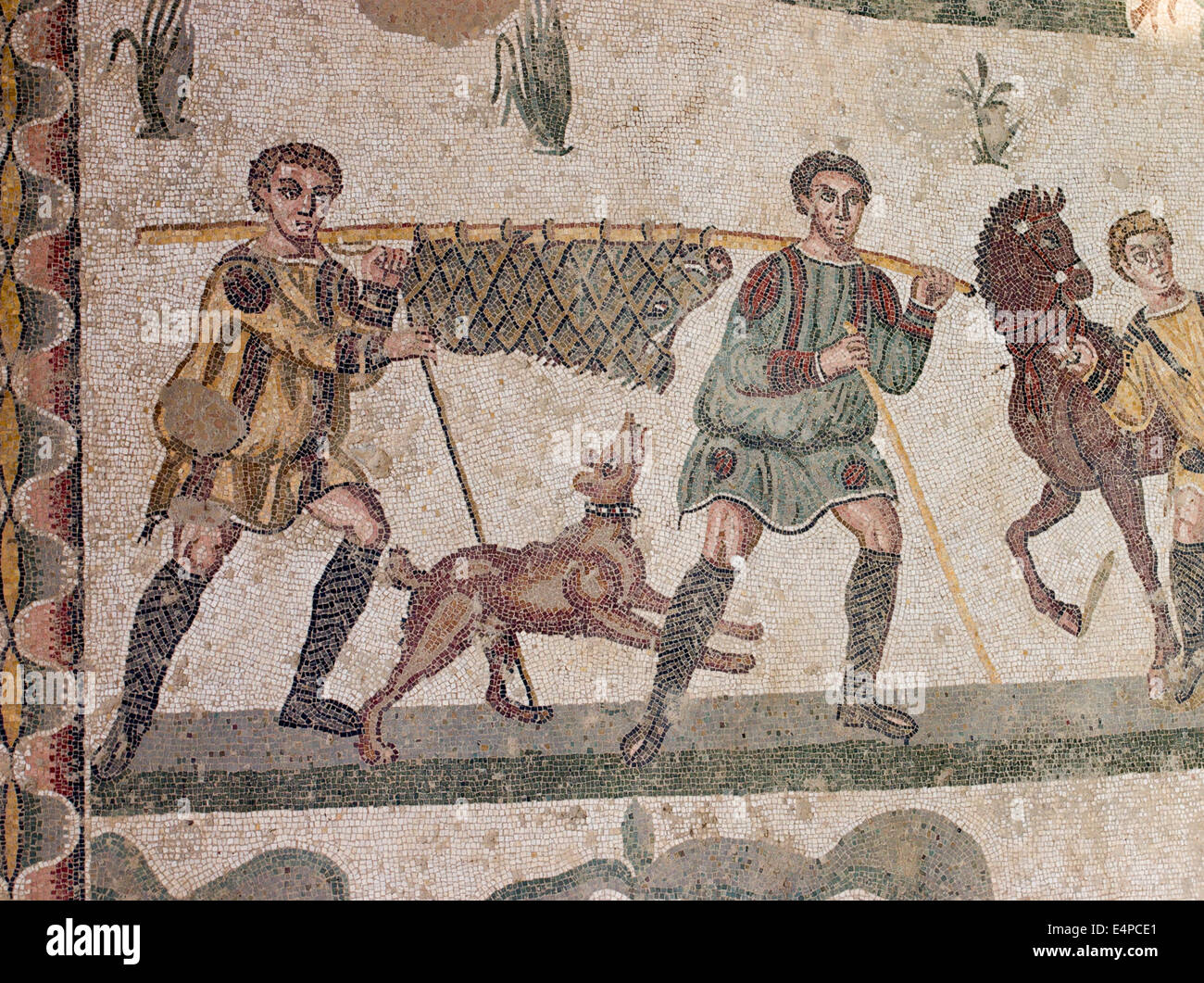 Nach der Jagd: den Eber nach Hause tragen. Zwei Männer tragen einen Stick mit einem erlegten Wildschwein eingewickelt im Inneren.  Ein Hund springt unten. Stockfoto