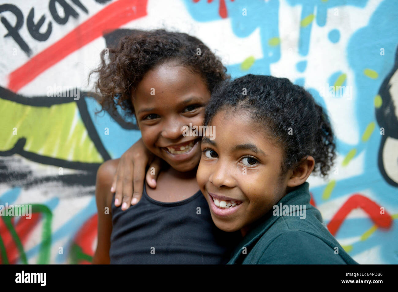 Zwei lächelnde Mädchen umarmen einander vor einer Wand mit Graffiti besprüht, Slum, Mangueirinha Favela, Duque De Caxias Stockfoto