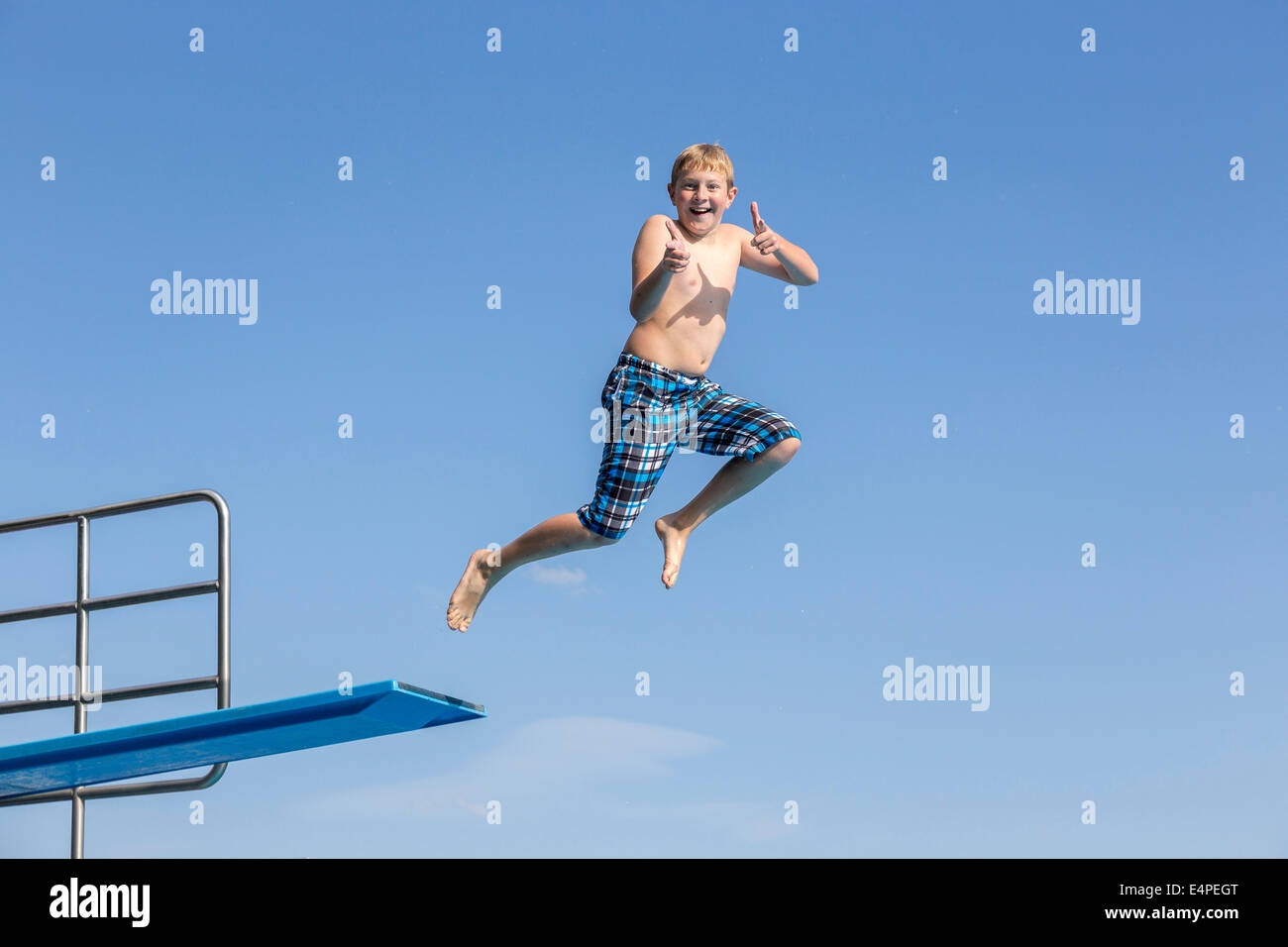 Junge, 10 Jahre, springen von einem drei-Meter-Brett macht ein Daumen hoch Geste Stockfoto