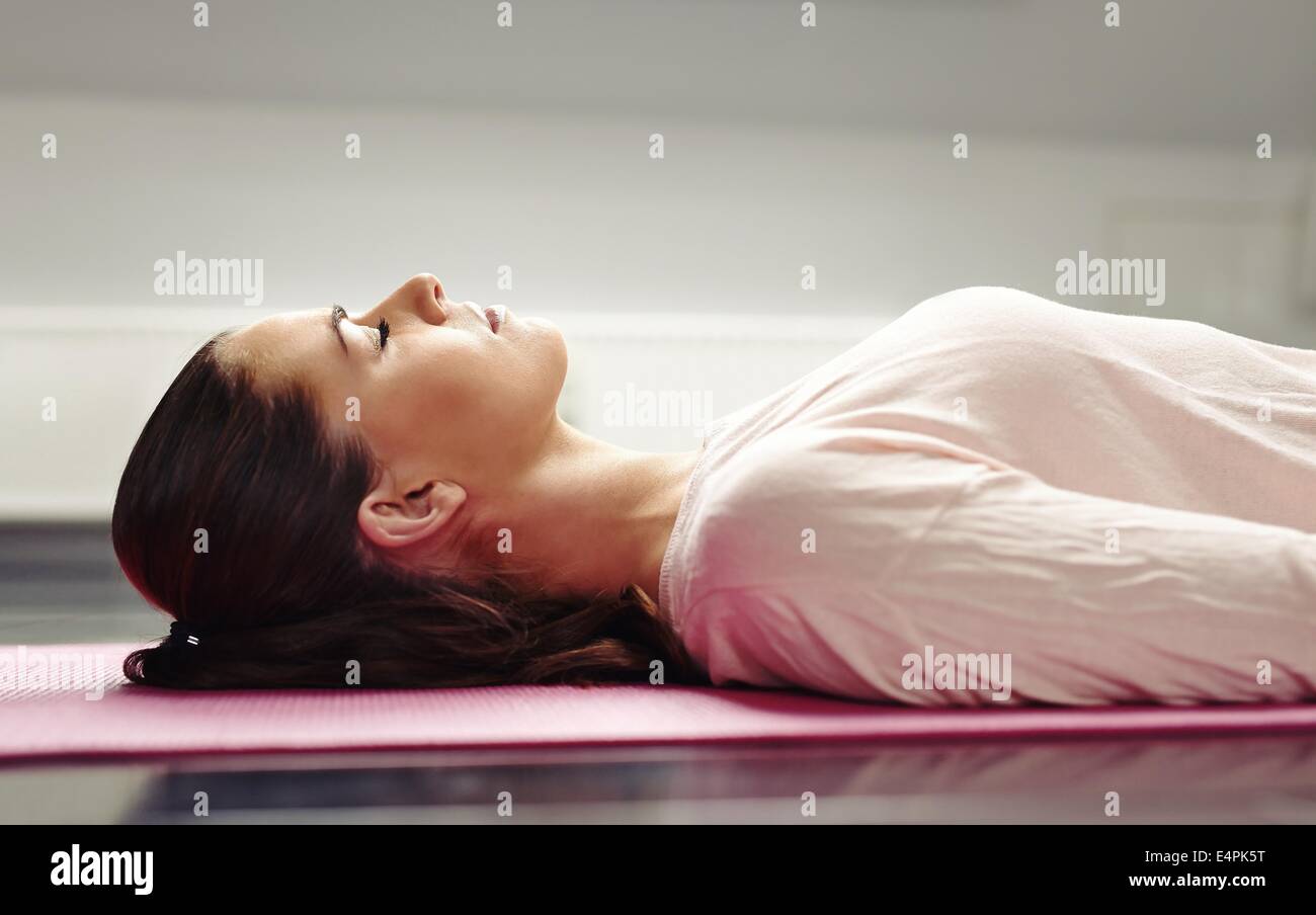 Schließen Sie herauf Bild der jungen Frau liegend auf einer Yogamatte mit ihren geschlossenen Augen in Meditation. Stockfoto