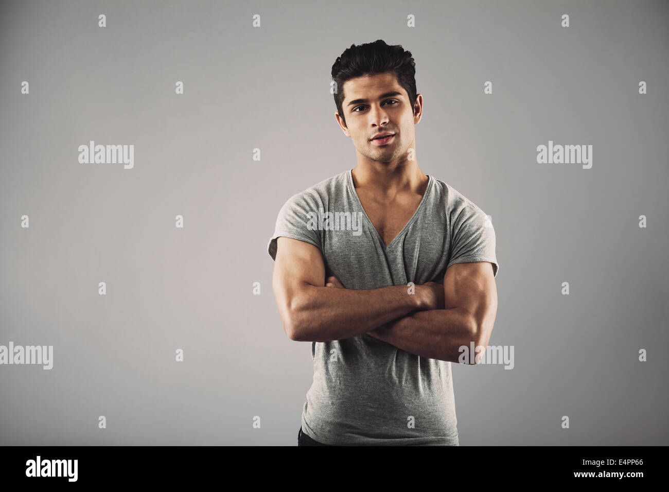 Porträt des jungen muskulöser Mann posiert vor grauem Hintergrund. Hübscher Junge hispanic Männermodel stehend mit seinen Armen gekreuzt Stockfoto