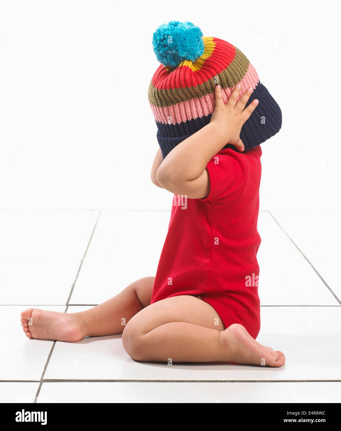 Baby Boy (16 Monate) mit bunten Streifen Woolly Hut über dem Kopf und Gesicht Stockfoto