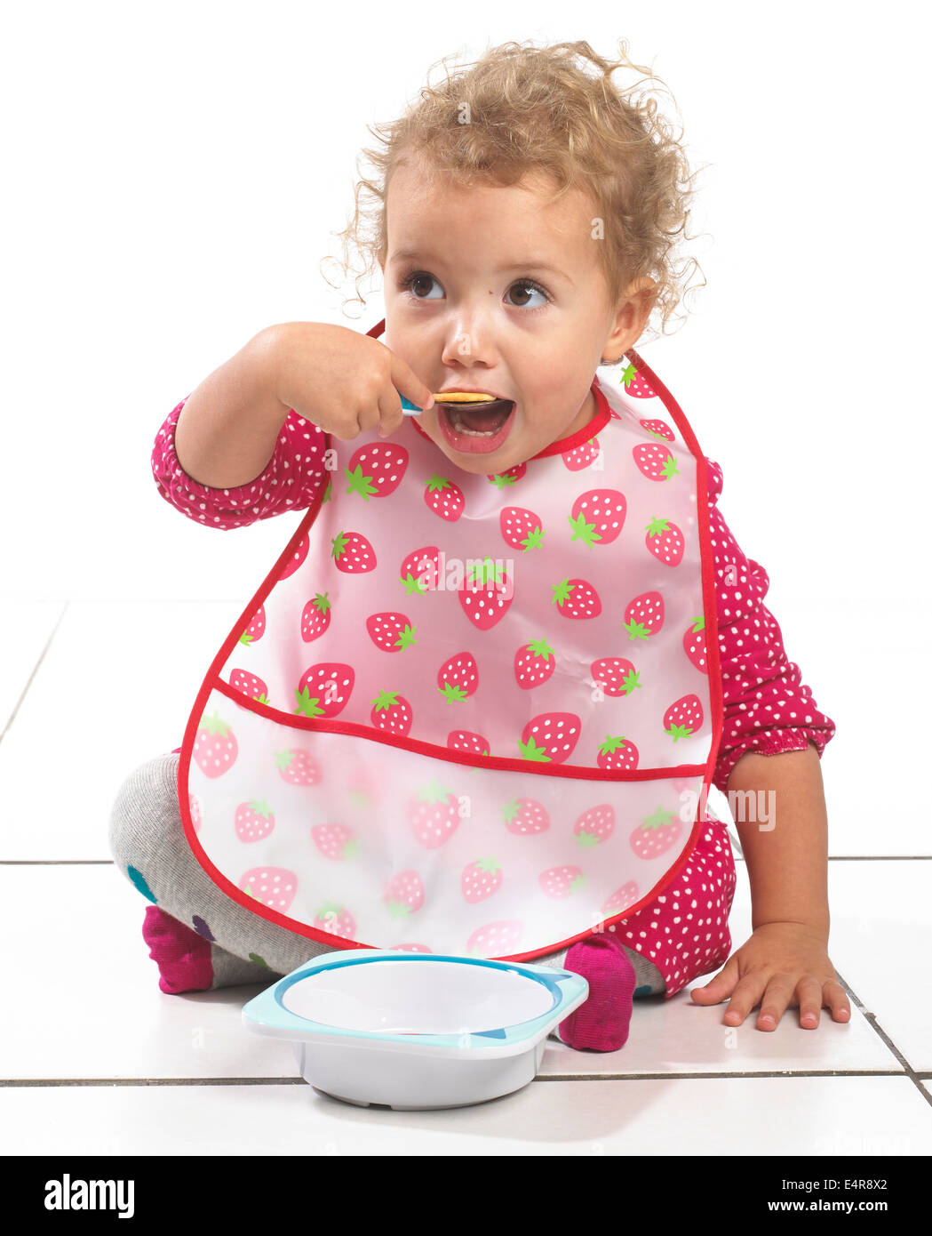 Mädchen (2 Jahre) trägt große Lätzchen aus Schüssel mit Löffel essen Stockfoto