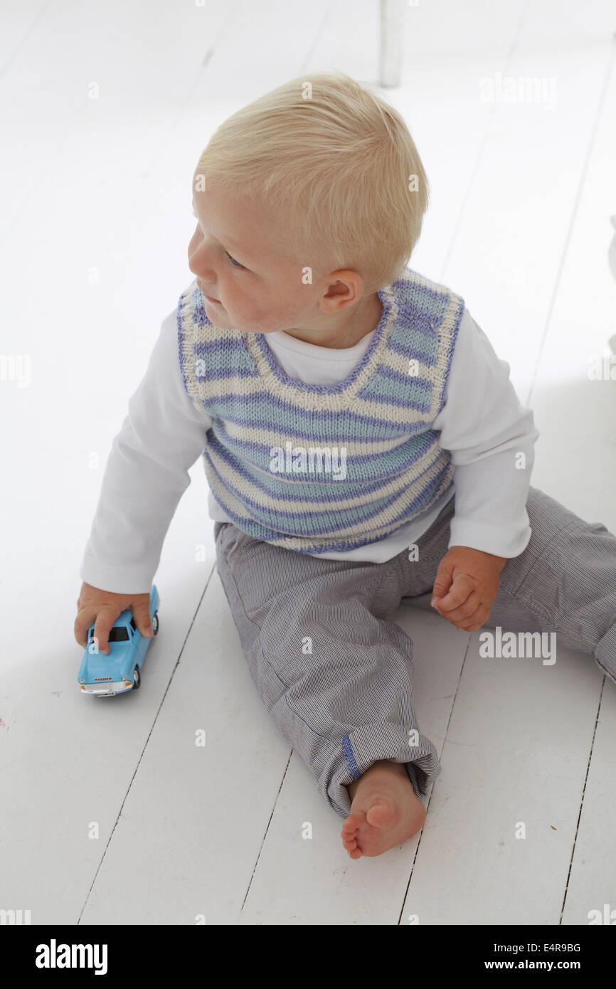 Baby Junge (14 Monate) sitzt auf weißen Holzboden hält ein Spielzeugauto Stockfoto