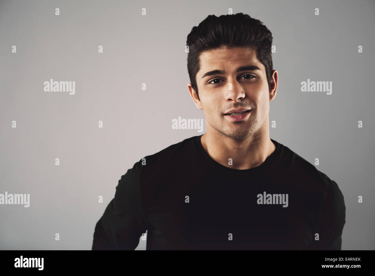 Horizontales Bild des jungen Mannes in lässigen t-Shirts, Blick in die Kamera. Hispanische junge Modell auf grauem Hintergrund mit Exemplar. Stockfoto