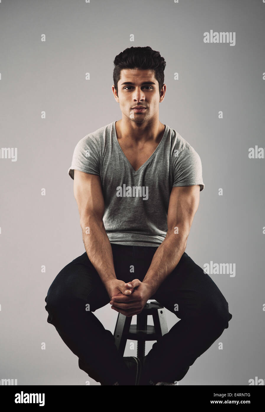 Porträt von muskulösen jungen männlichen Models auf Hocker sitzend. Hispanische Jüngling auf grauem Hintergrund. Stockfoto