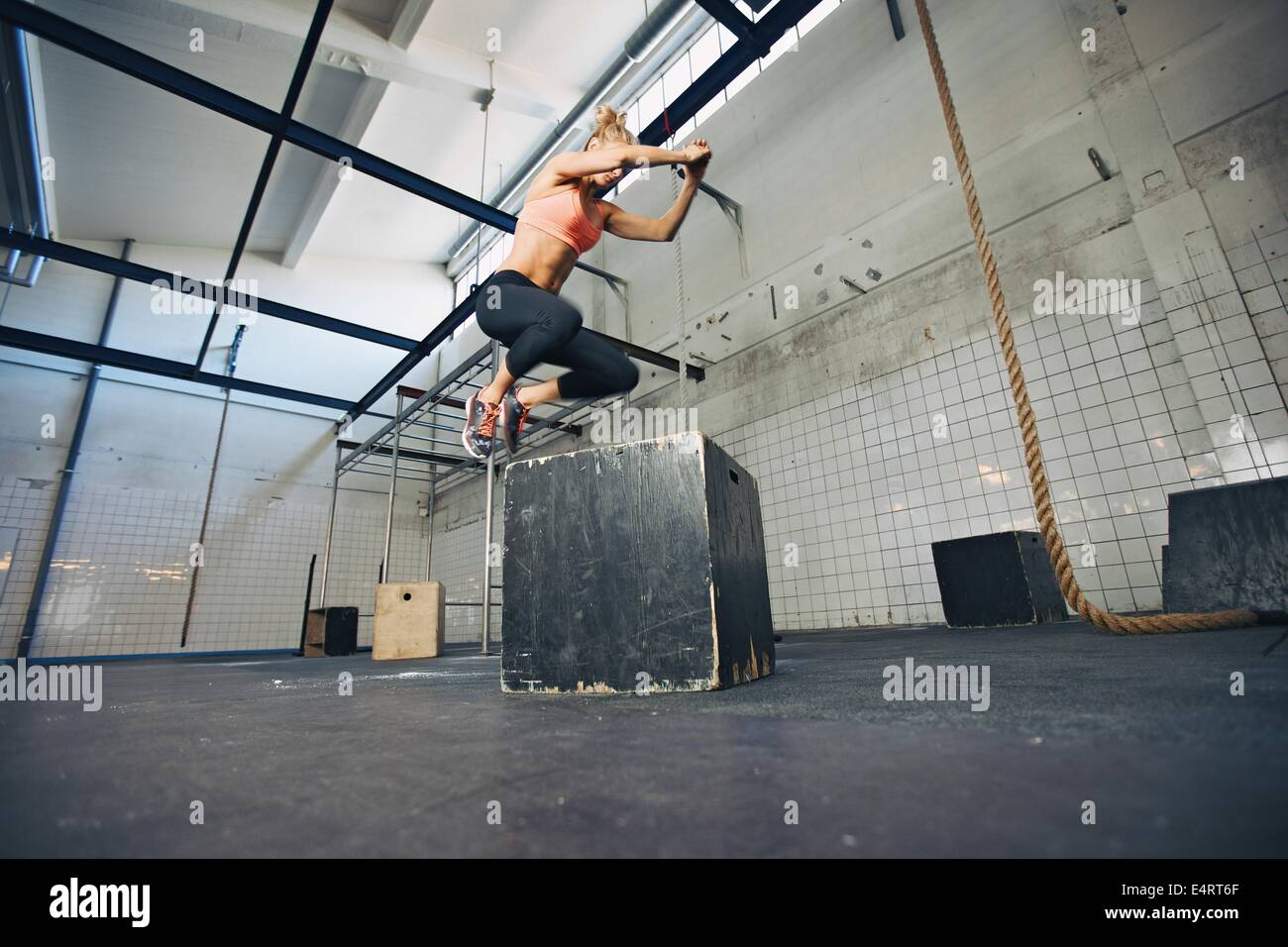 Niedrigen Winkel Ansicht der jungen Sportlerin Box springen in einem Crossfit Gym. Fit Woman ist Feld Sprünge im Fitnessstudio durchführen. Stockfoto