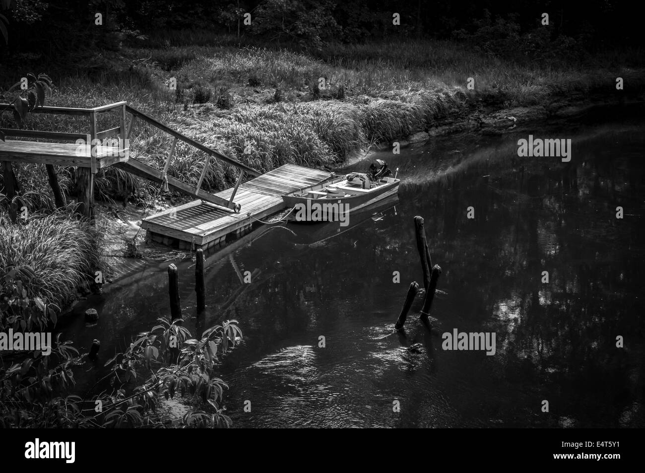 An diesem sehr heißen Sommertag sitzt ein kleines Boot friedlich komfortalbel zum Dock, wie das Wasser in diesem Gezeiten-Fluss, ins Meer fließt. Stockfoto