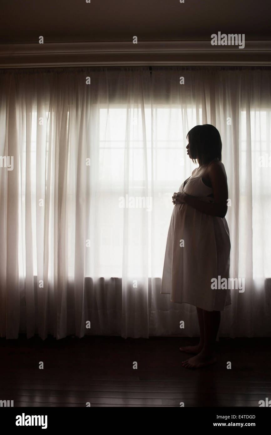 Silhouette der schwangeren Frau schaut aus Fenster Stockfoto