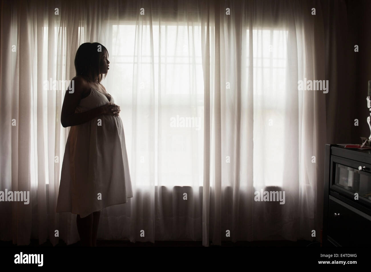 Silhouette der schwangeren Frau schaut aus Fenster Stockfoto