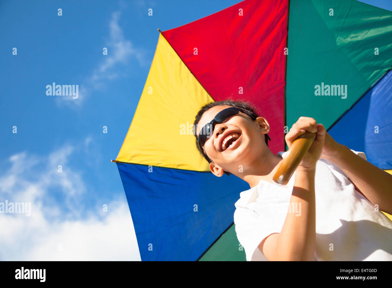 kleiner Junge glücklicher halten einen bunten Regenschirm mit blauem Himmel Stockfoto
