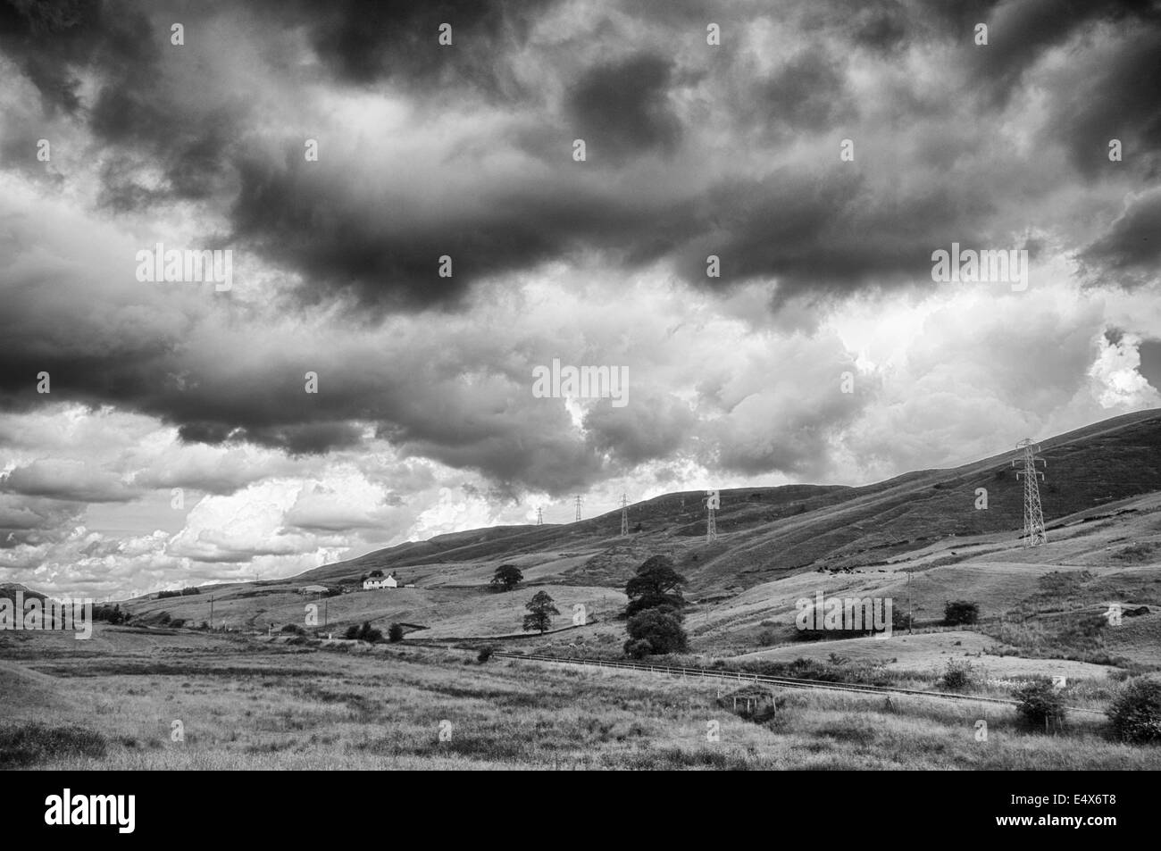 Stimmungsvolle schwarz-weiß Landschaft mit Bauernhaus, Elektrokabel Pylonen und eine Bahnstrecke Stockfoto