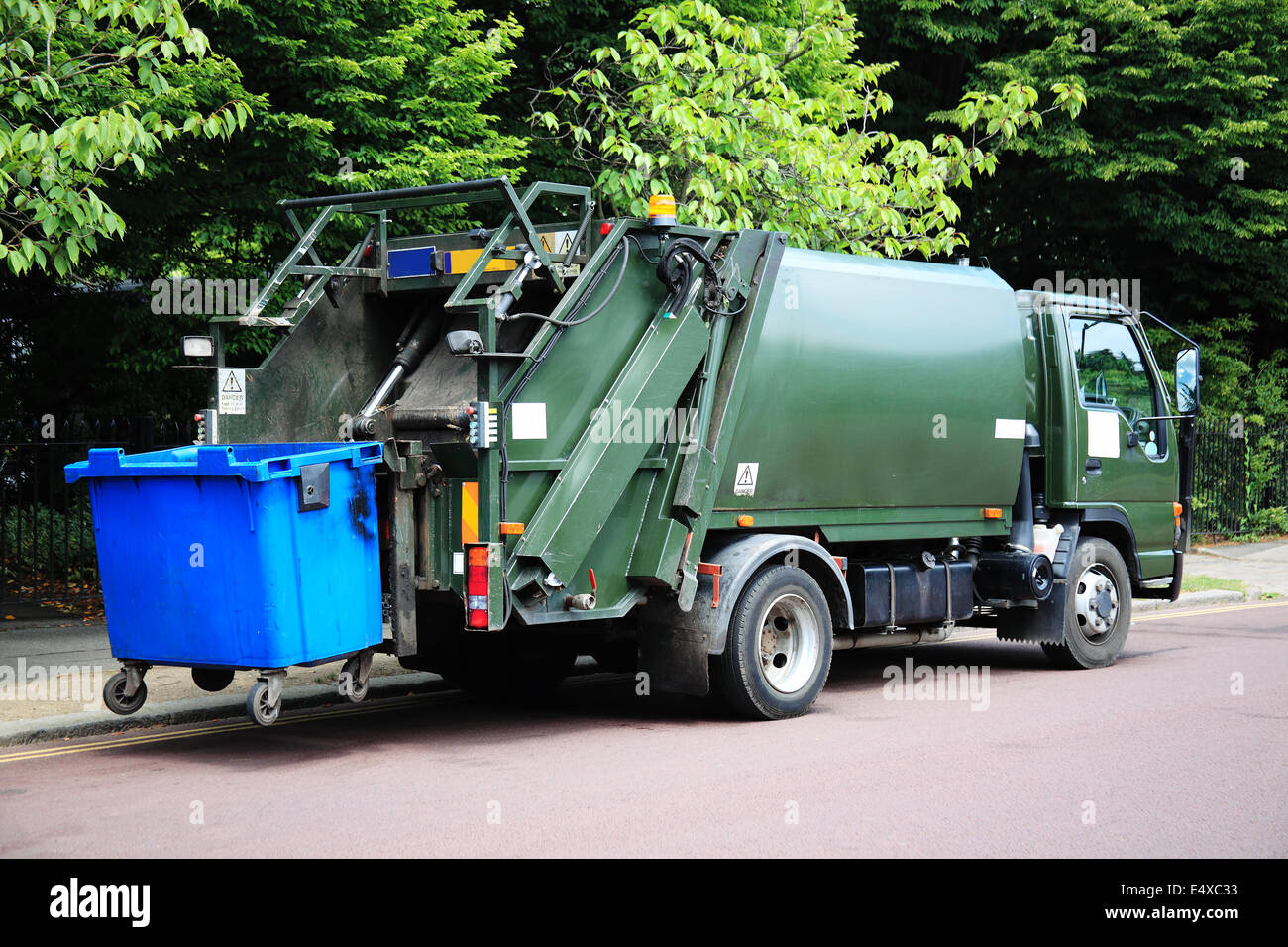Grüne Müllwagen mit einer erhöhten blauen Wheelie bin am Heck Stockfoto