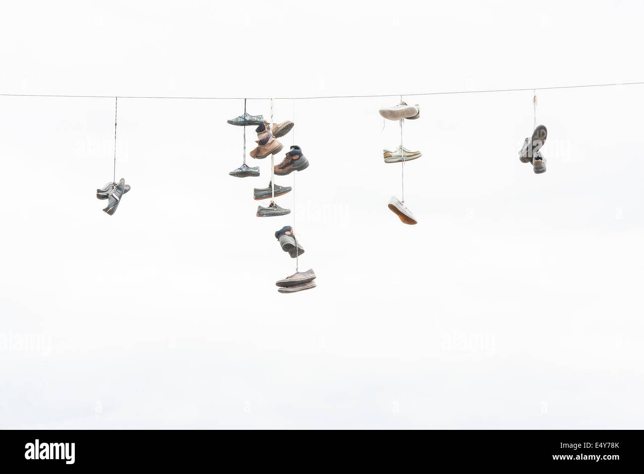 Viele alte abgenutzte Stiefel oder Schuhe, die an ein elektrisches Kabel hängen Stockfoto