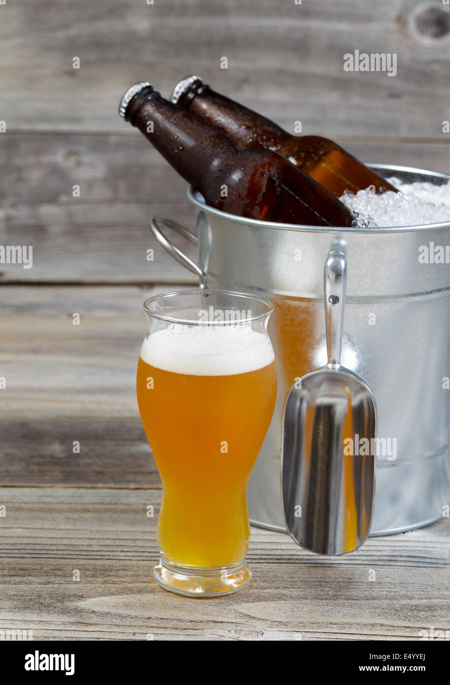 Vertikale Ansicht von einem frisch Gießen gold Bier mit Flaschenbier sitzen in Blecheimer gefüllt mit crushed Eis und rustikal Holz Stockfoto
