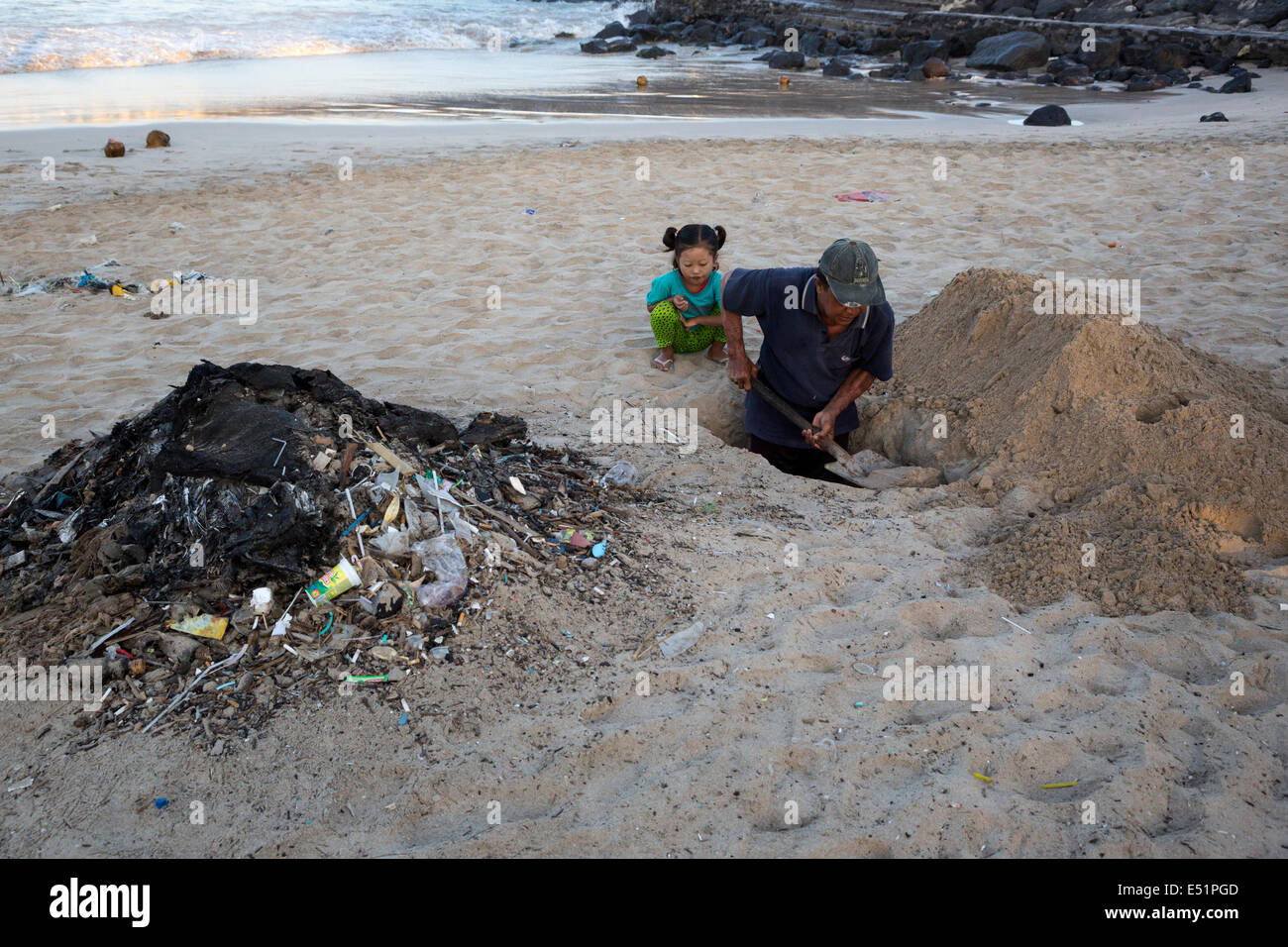 Jimbaran, Bali, Indonesien.  Man gräbt eine Grube am Strand Müll begraben. Stockfoto