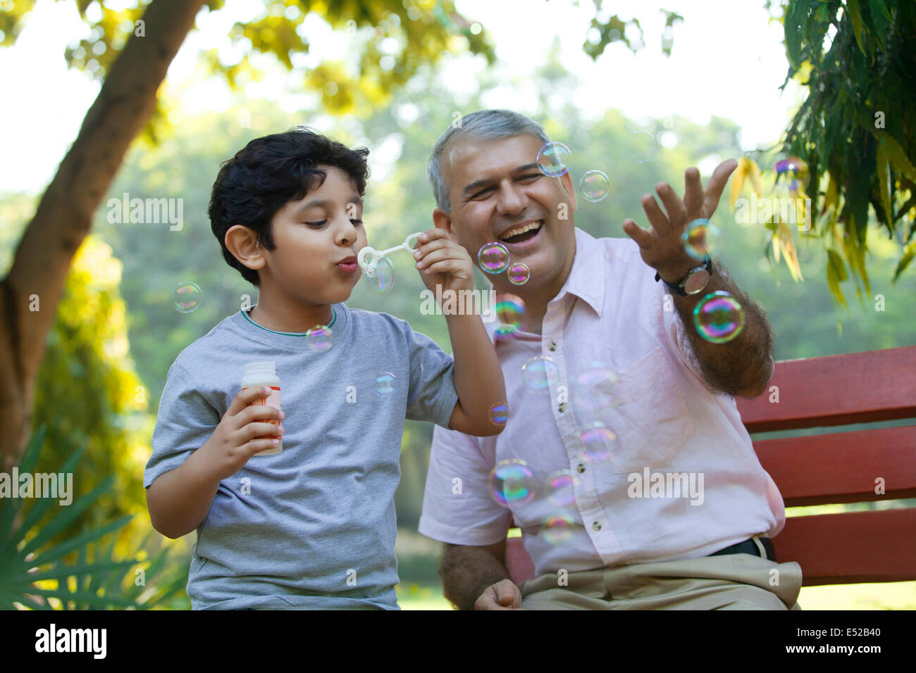 Boy bläst Seifenblasen in einem Park, während Großvater schaut Stockfoto