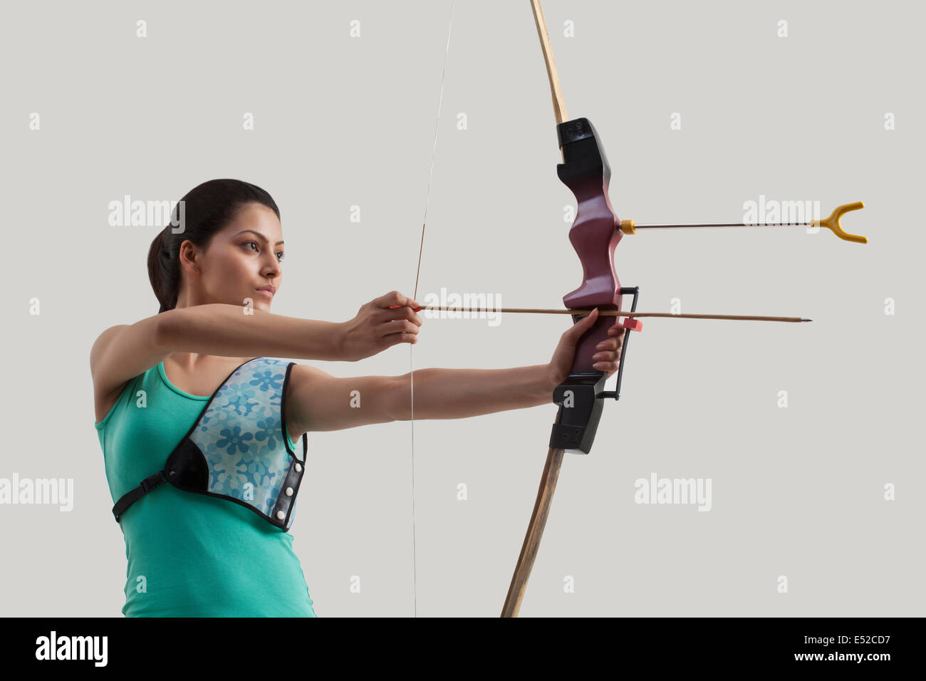 Junge weibliche Bogenschütze mit Pfeil und Bogen gegen grauen Hintergrund Stockfoto