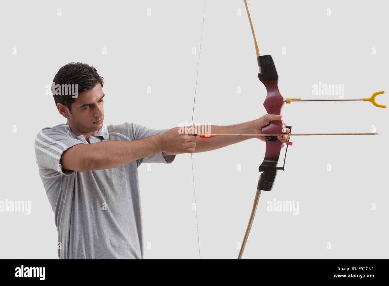 Männliche Schütze mit dem Ziel, Pfeil und Bogen gegen grauen Hintergrund Stockfoto