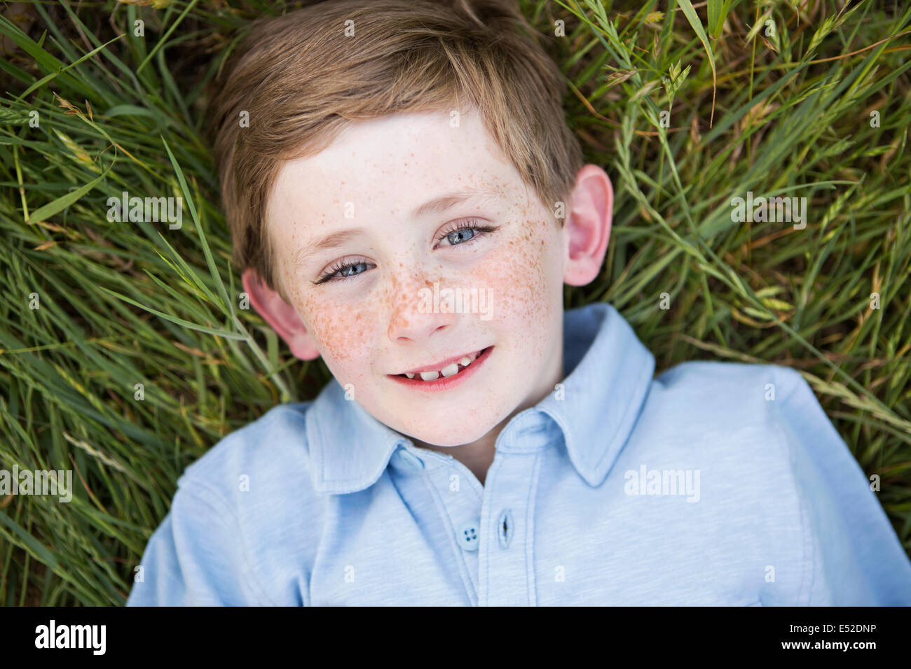Ein Junge in ein blaues Hemd, auf dem Rücken auf dem Rasen liegend. Stockfoto