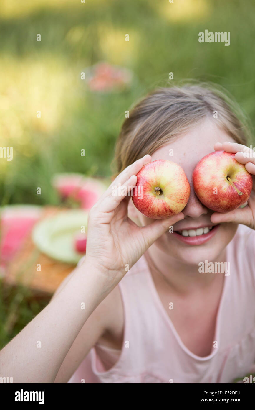 Ein Mädchen hält zwei Äpfel vor ihren Augen Stockfoto