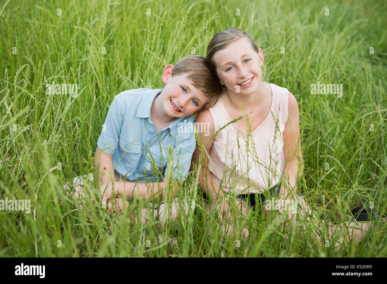 Bruder und Schwester sitzen nebeneinander, langes Gras. Stockfoto