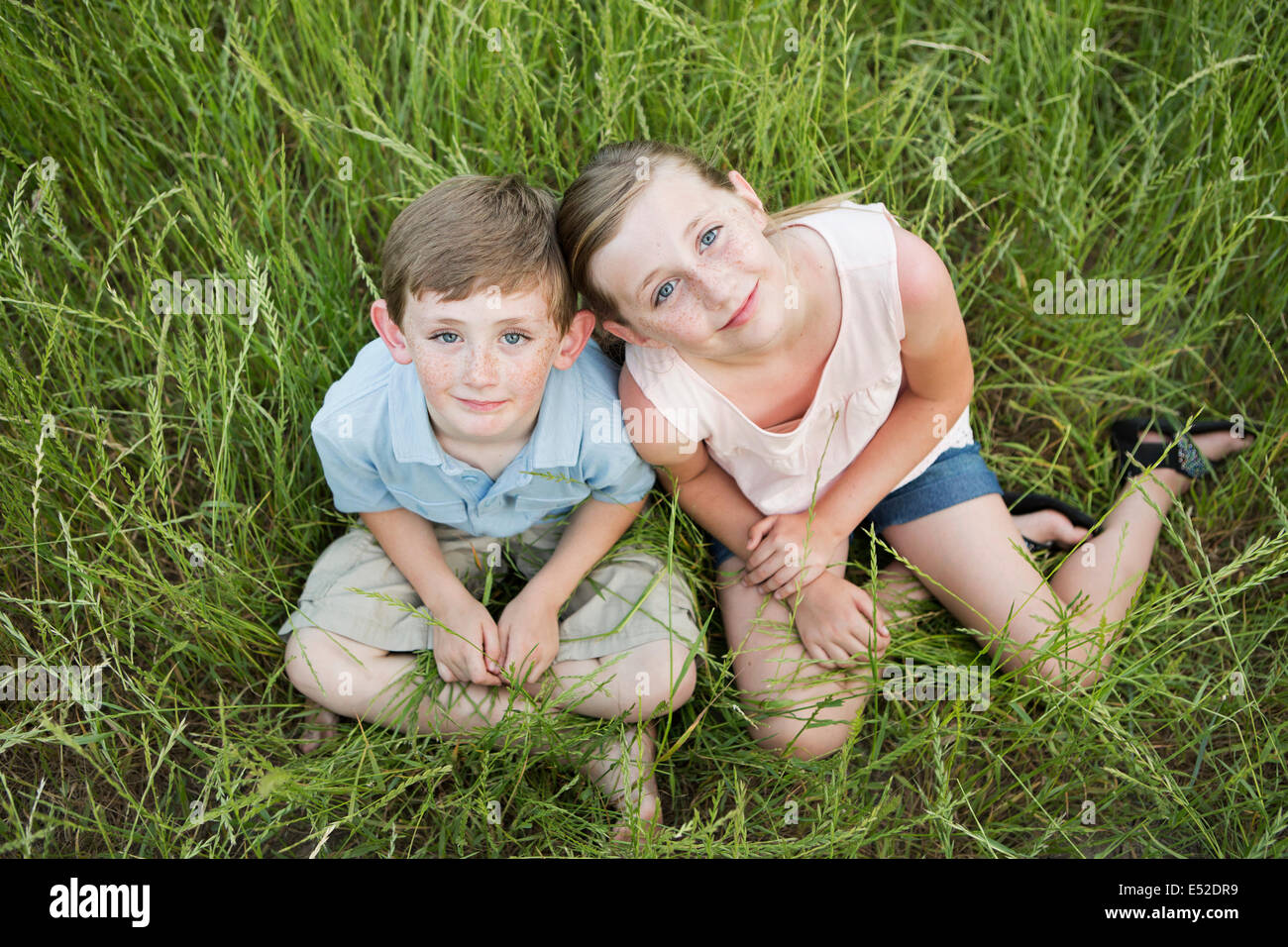 Bruder und Schwester sitzen nebeneinander, langes Gras. Stockfoto